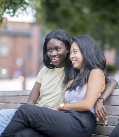 An interracial couple is siting on a park bench. They are embracing and enjoying the day.